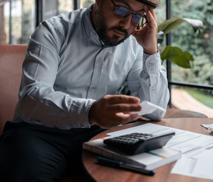Man in glasses calculating expenses with a receipt and calculator, illustrating ways people lose money while saving.