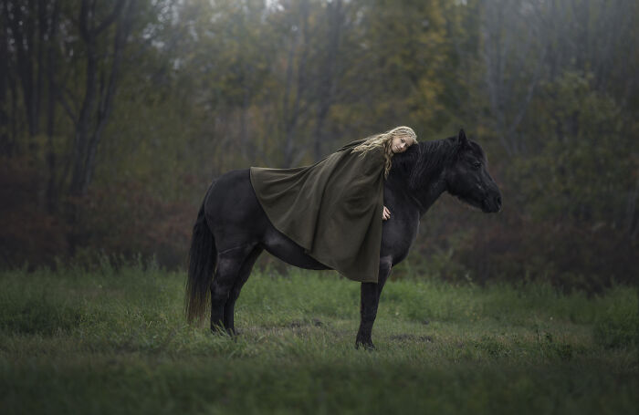Child lying on a black horse in a serene forest, capturing the magical bond between children and animals in a whimsical portrait.