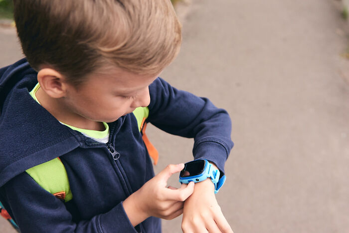 Young boy wearing a blue jacket checking his blue smartwatch outdoors, reflecting on soul-crushing things parents told him.