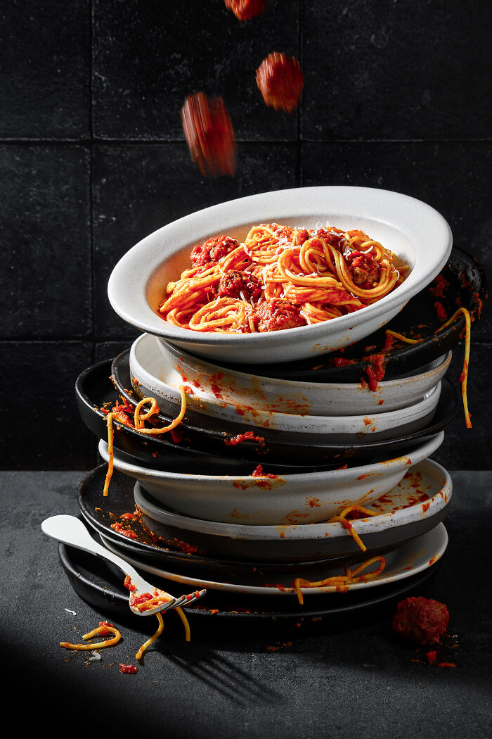 Stack of plates with messy spaghetti and meatballs, captured in a creative food photography shot for World Food Photography Awards.