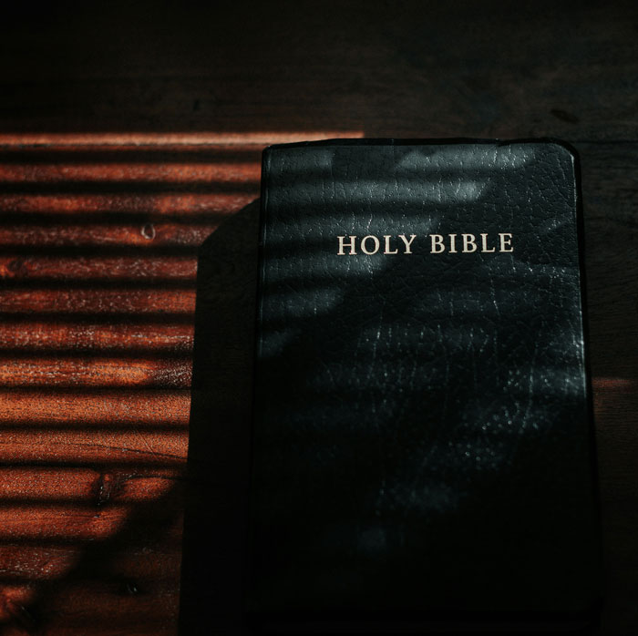 Black Holy Bible on wooden table with striped shadow, related to people who escaped from cults sharing experience.