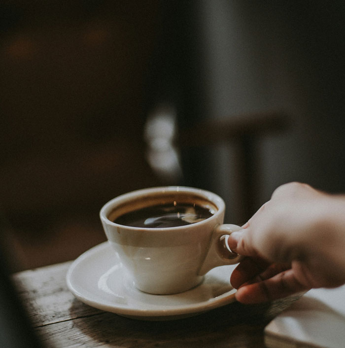 A hand holding a white coffee cup on a saucer, symbolizing reflection on friendship of 10+ years ended.