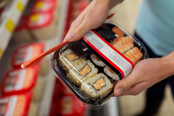 Person holding packaged sushi in a store aisle, highlighting wild cooking opinions about popular food choices online.