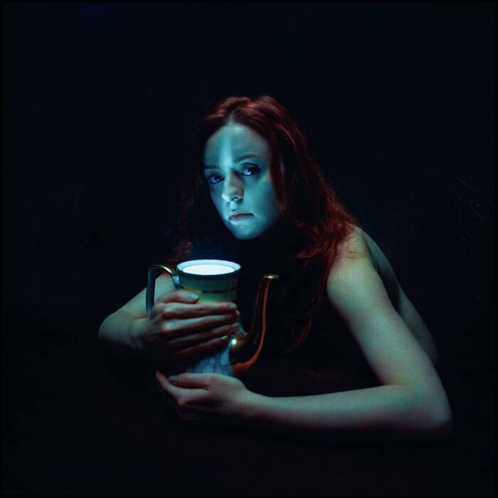 Woman holding a glowing vintage pitcher in dark setting, captured in an intimate, cinematic-looking shot by a photographer.