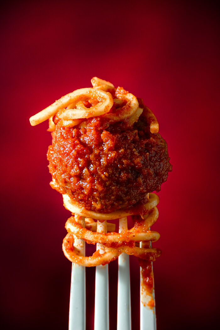 Fork holding a meatball wrapped in spaghetti with rich tomato sauce, a stunning food photography award-winning shot.