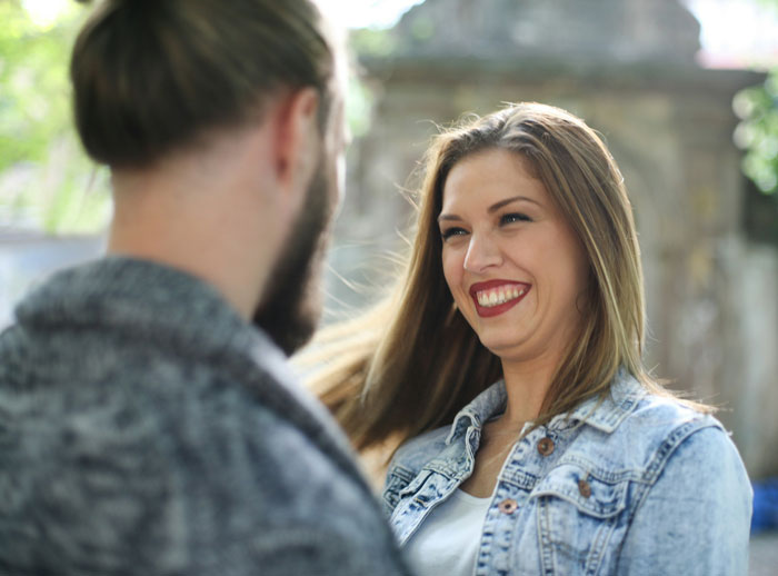 A woman smiling while talking to a man outdoors, illustrating problematic behaviors women get a pass for.
