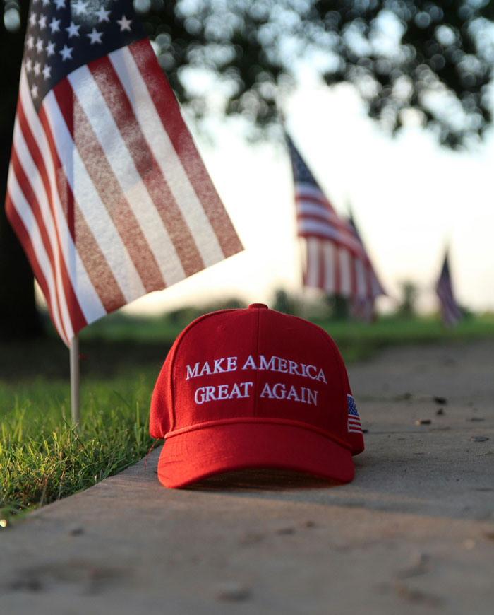 Red Make America Great Again hat on pavement near American flags, symbolizing themes from people who escaped from cults.