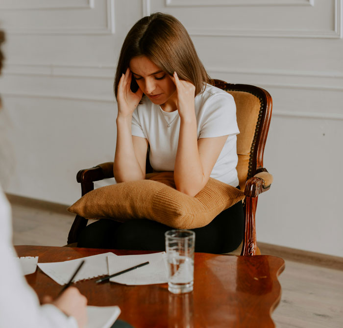 Young woman sitting with a pillow, holding her head stressed, symbolizing bosses and teachers going off the rails.