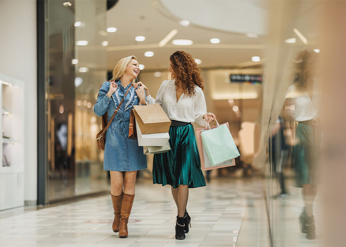 Two women happily walking and carrying shopping bags, illustrating things everyone does but doesn’t talk about.