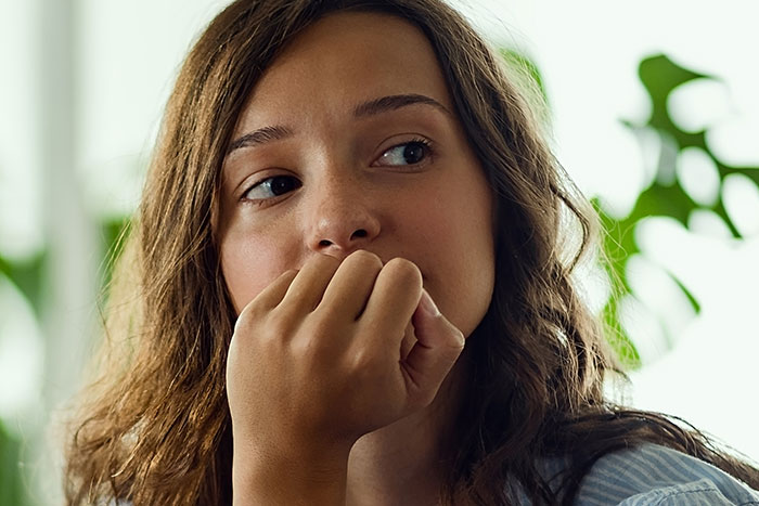 Young woman with anxious expression and hand near mouth, portraying a gut feeling of needing to leave immediately.