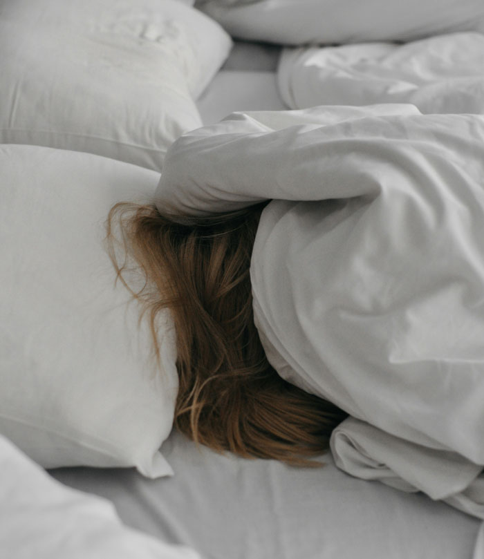 Person hiding under white blanket in bed, representing one weird parent rule thought normal until older.