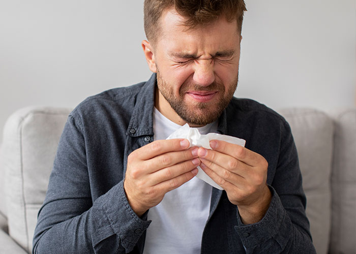 Man with a painful expression holding a tissue, illustrating a scene of a pathetic injury or discomfort at home.