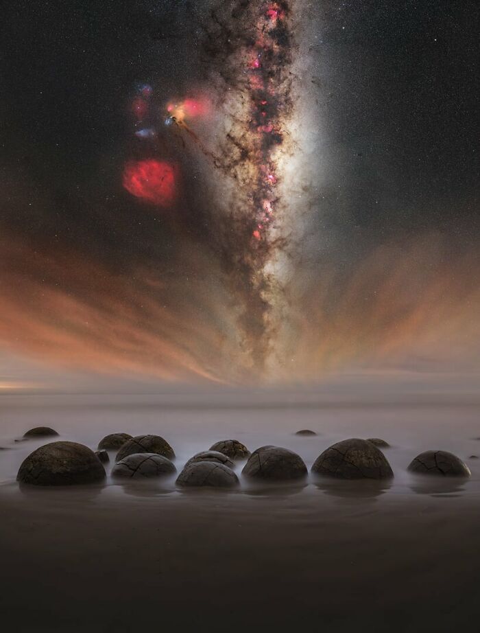 Milky Way shining brightly over rounded boulders on a misty beach under the clear night sky.