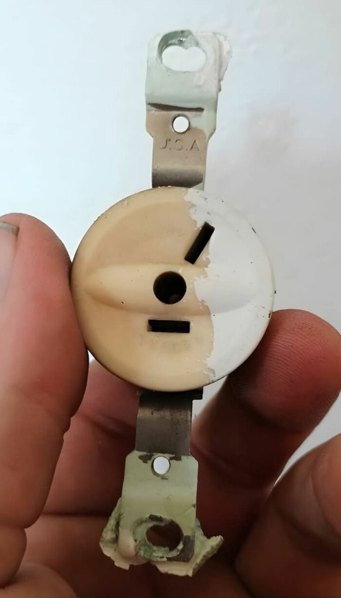 Hand holding a vintage electrical outlet showing wear and discoloration found in homes with hidden haunted pasts.