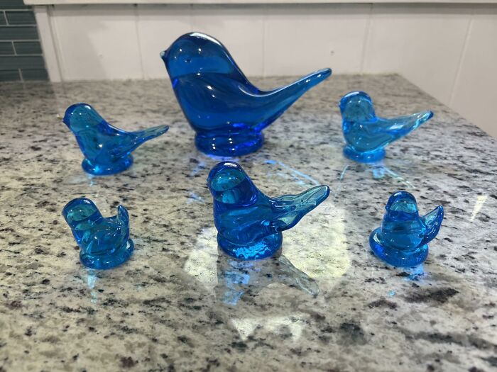 Six bright blue glass bird figurines arranged on a speckled granite countertop, showcasing thrifted finds.