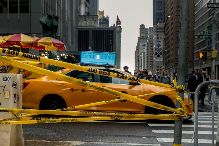 Yellow taxi cab behind caution tape on busy city street, capturing urban life for Pure Street Photography Grant winners.
