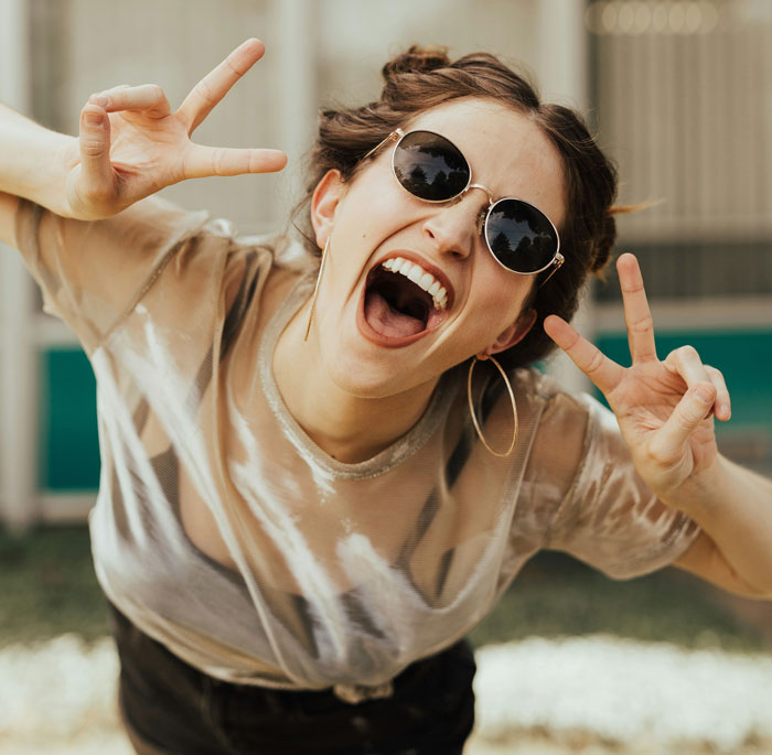 Young woman wearing sunglasses, smiling and making peace signs, representing problematic behaviors women get a pass for