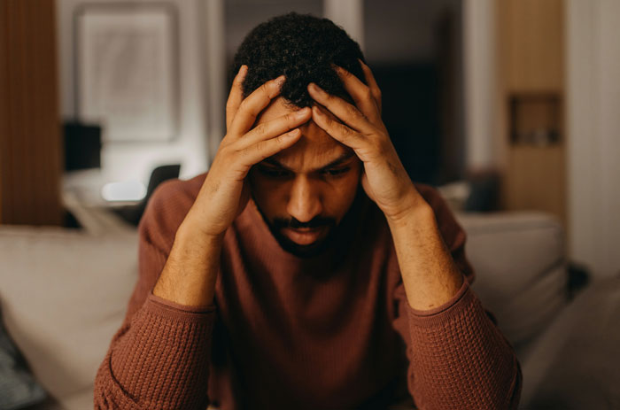 Man sitting on couch holding head with hands, appearing worried, illustrating spouse secrets kept after marriage concept