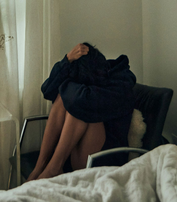 Person sitting curled up on a chair in a dimly lit room, reflecting the emotional impact of escaping from cults.