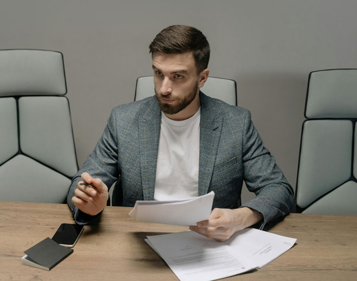 Man in a gray blazer reviewing documents at a conference table, representing people in charge in leadership roles.