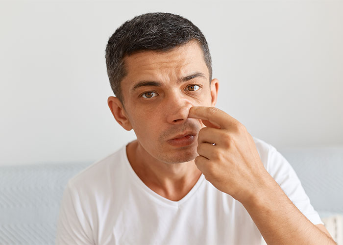 Man in a white shirt picking his nose, illustrating things everyone does but doesn't talk about in daily life.