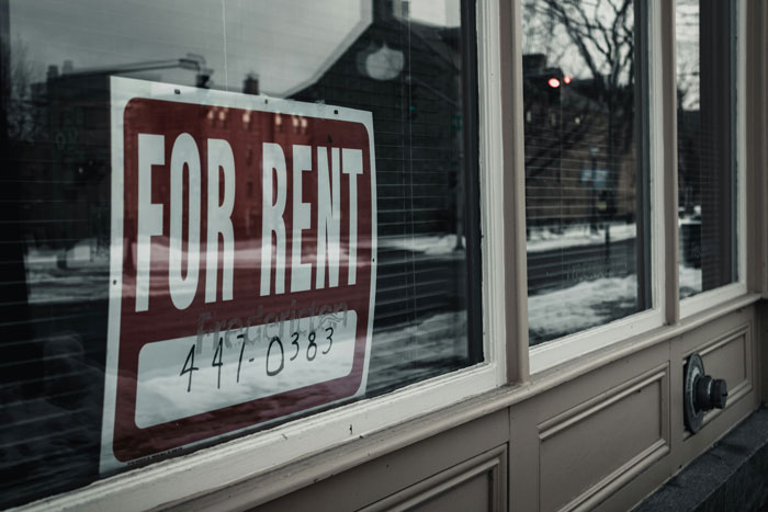 For rent sign on a window reflecting a street, illustrating common ways people lose money while thinking they’re saving.