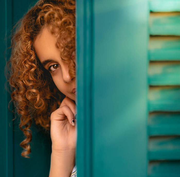 Woman with curly hair peeking from behind green shutters, illustrating problematic behaviors women get a pass for according to men