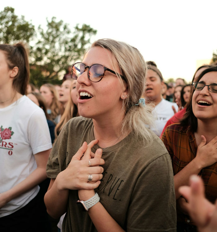 Young woman with glasses feeling emotional surrounded by a crowd, illustrating stories from people who escaped from cults.