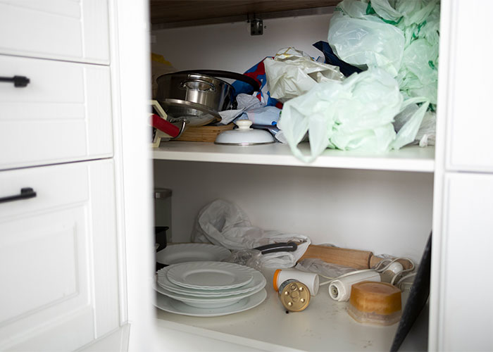 Cluttered kitchen cabinet with dishes, plastic bags, and kitchen tools, showing things everyone does but doesn’t talk about.
