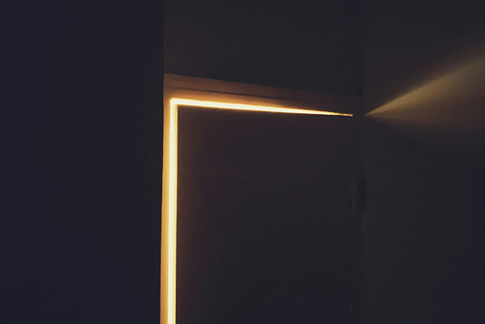 Dimly lit door slightly open with bright light shining through, evoking a scary gut feeling to leave immediately.