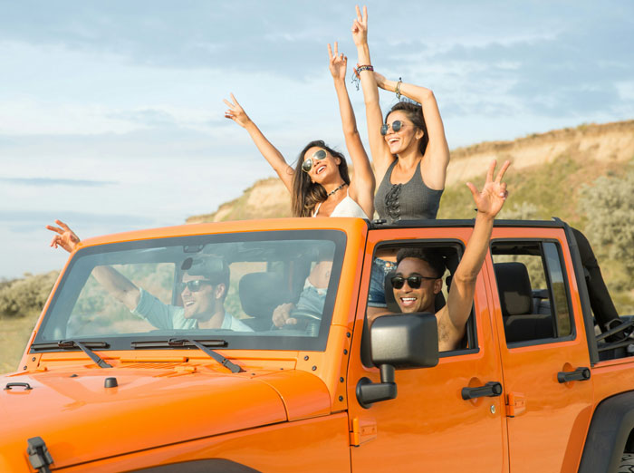 Four friends with sunglasses enjoying a road trip in an orange jeep, symbolizing long-term friendship moments.