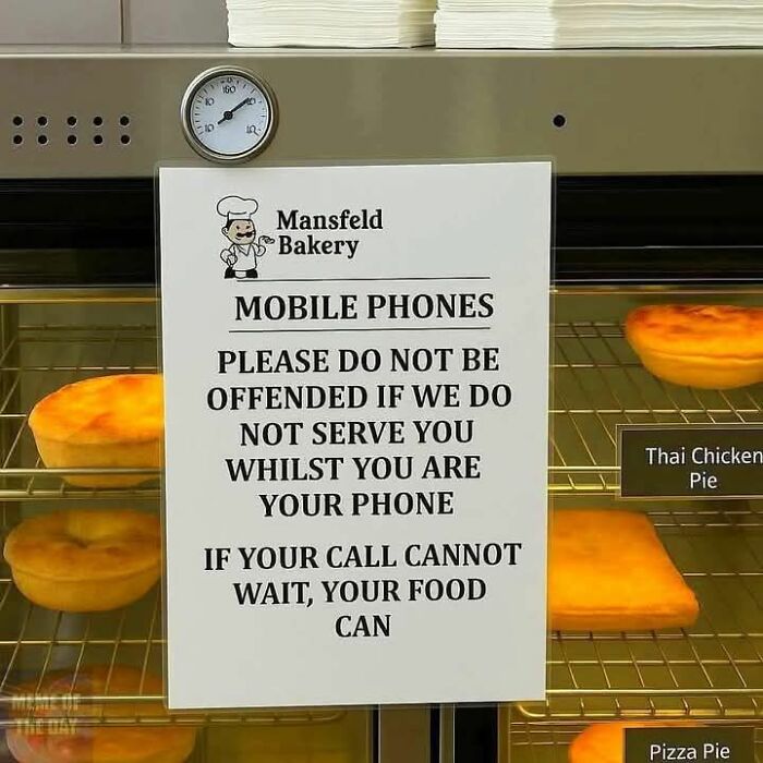 Sign in a bakery humorously warning customers on mobile phones that food service may be delayed, relatable hospitality meme.