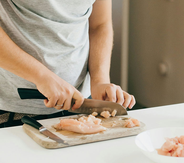 Person cutting raw chicken on a board, symbolizing former employees revealing disturbing workplace secrets after quitting jobs