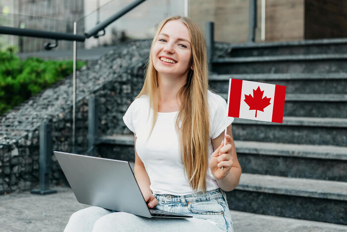 Young woman holding Canadian flag and using laptop outdoors, symbolizing small decision that unexpectedly changed life forever.