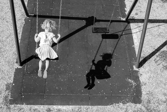 Young child on a swing casting a clear shadow in a black and white pure street photography scene.