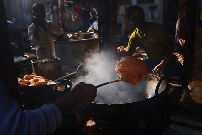 Street vendor frying traditional Indian food with steam rising, showcasing award-winning world food photography artistry.