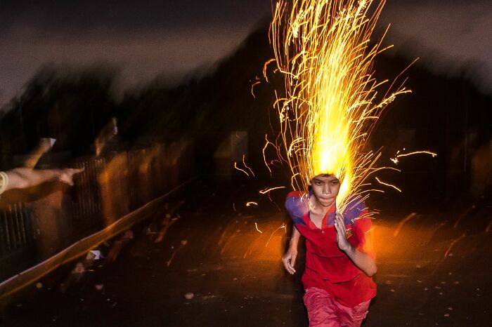 Young boy running at night with fireworks exploding above his head, captured in pure street photography style.