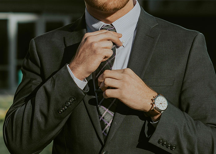 Man adjusting tie wearing full suit at office symbolizing employee standing up to boss and getting him demoted
