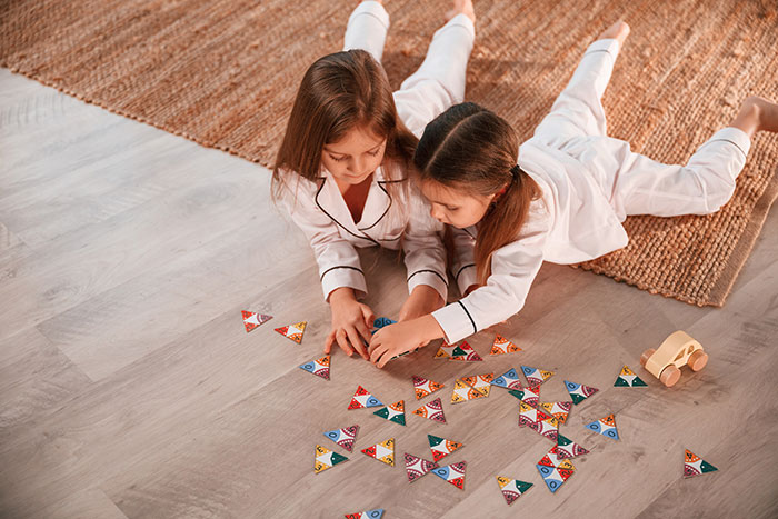 Two young girls in pajamas playing on the floor with toys, highlighting furniture damage and friend disputes.