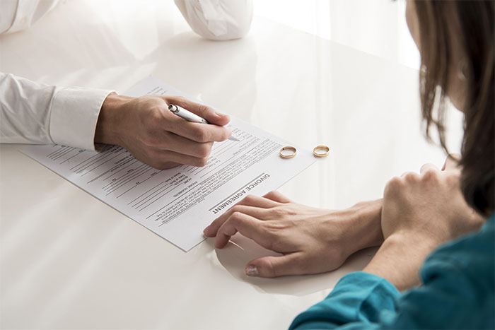 Couple discussing divorce agreement with wedding rings on table, relating to dropping baby off with ex-husband.