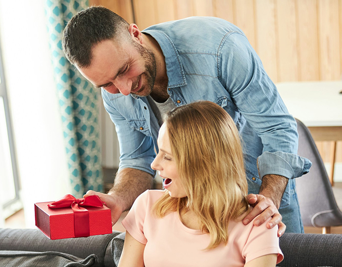 Man handing a gift to his surprised pregnant wife who he does not yet consider a mom for Mother&rsquo;s Day.