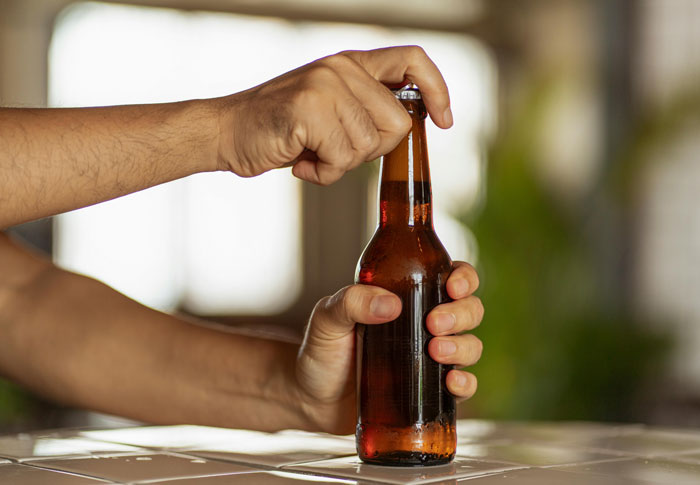 Hands opening a brown glass beer bottle, illustrating roommate blamed for tempting a teen who steals alcohol from their room. Hands opening a brown glass beer bottle, illustrating roommate blamed for tempting a teen who steals alcohol from their room.