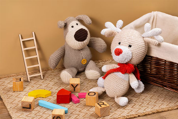 Crocheted dog and reindeer toys with scattered wooden letter blocks and a small wooden ladder on a woven mat. Crocheted dog and reindeer toys with scattered wooden letter blocks and a small wooden ladder on a woven mat.
