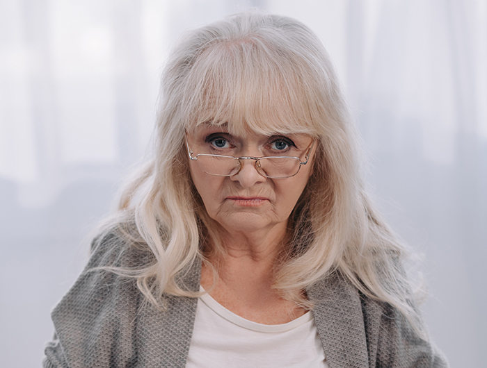 Elderly woman with glasses looking stern, representing challenges in hiding wealth from dysfunctional families. Elderly woman with glasses looking stern, representing challenges in hiding wealth from dysfunctional families.