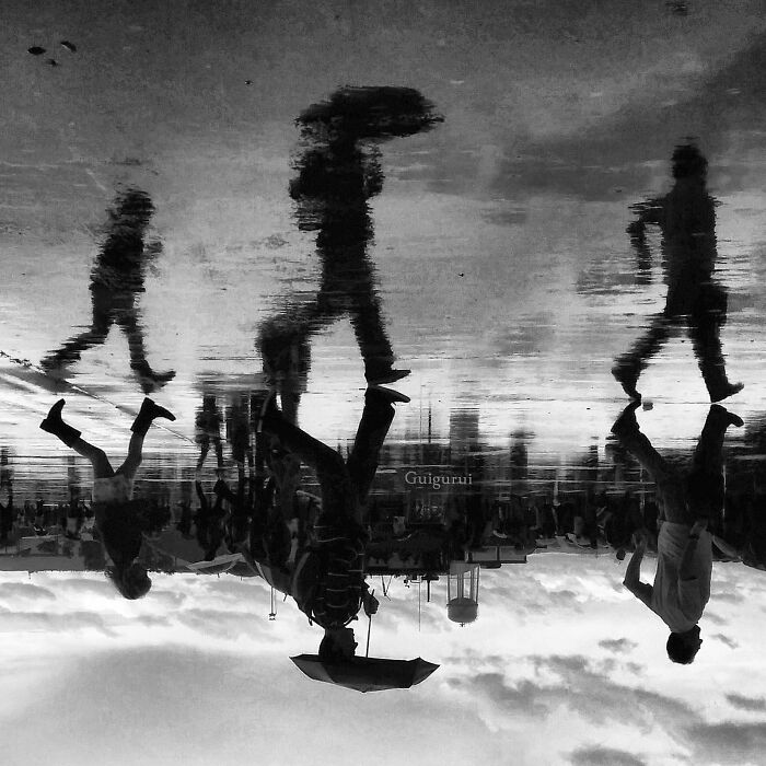 Reflections of people walking on a wet street, capturing dynamic street photography moments in an urban environment.