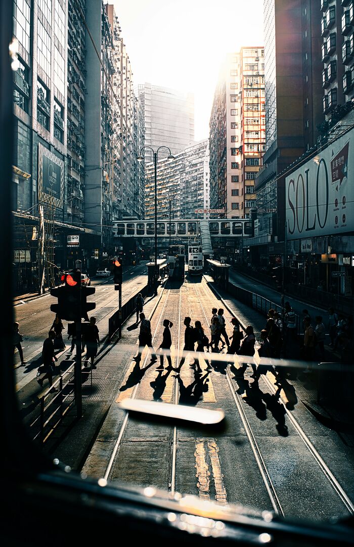Busy urban street scene with pedestrians crossing and tram tracks, highlighting street photography moments in a cityscape.
