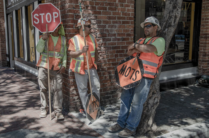 Three construction workers in safety vests holding stop signs on a city sidewalk, highlighting street photography moments.