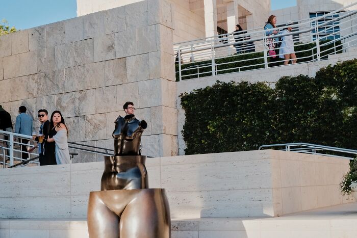 Street photography moment showing people near a modern sculpture in an urban public space under clear sky.
