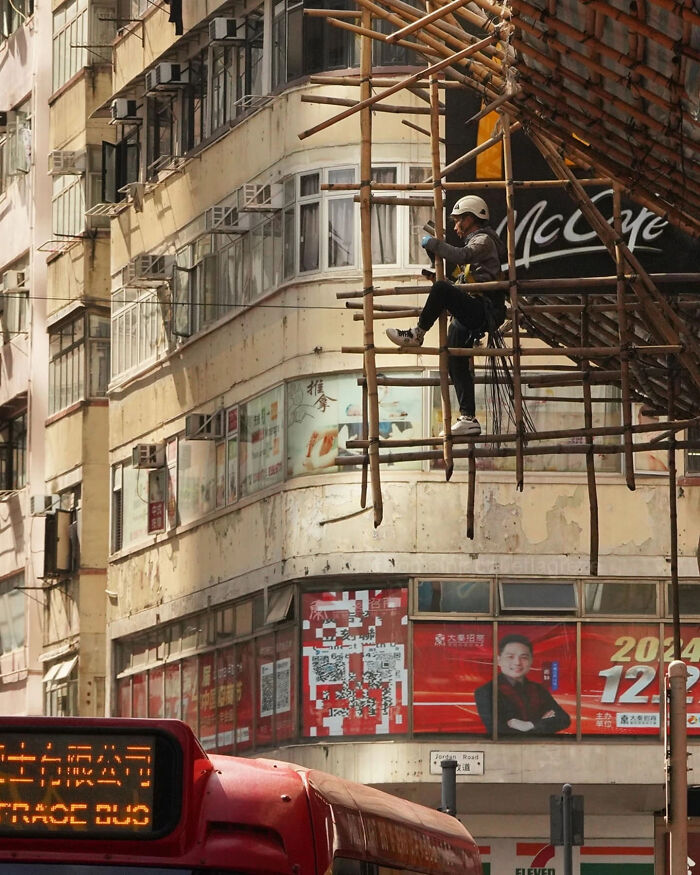 Construction worker on bamboo scaffolding in an urban scene, a classic moment in street photography captured by talented photographers.