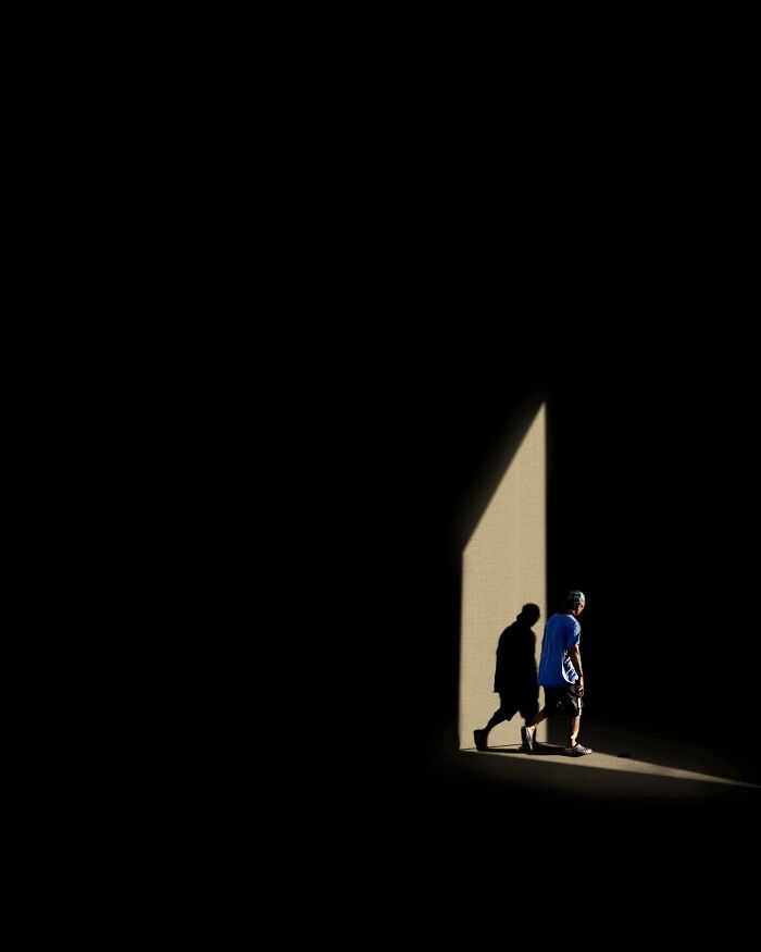 Man walking through a sharp light beam casting a shadow in a dark urban scene, a striking street photography moment.